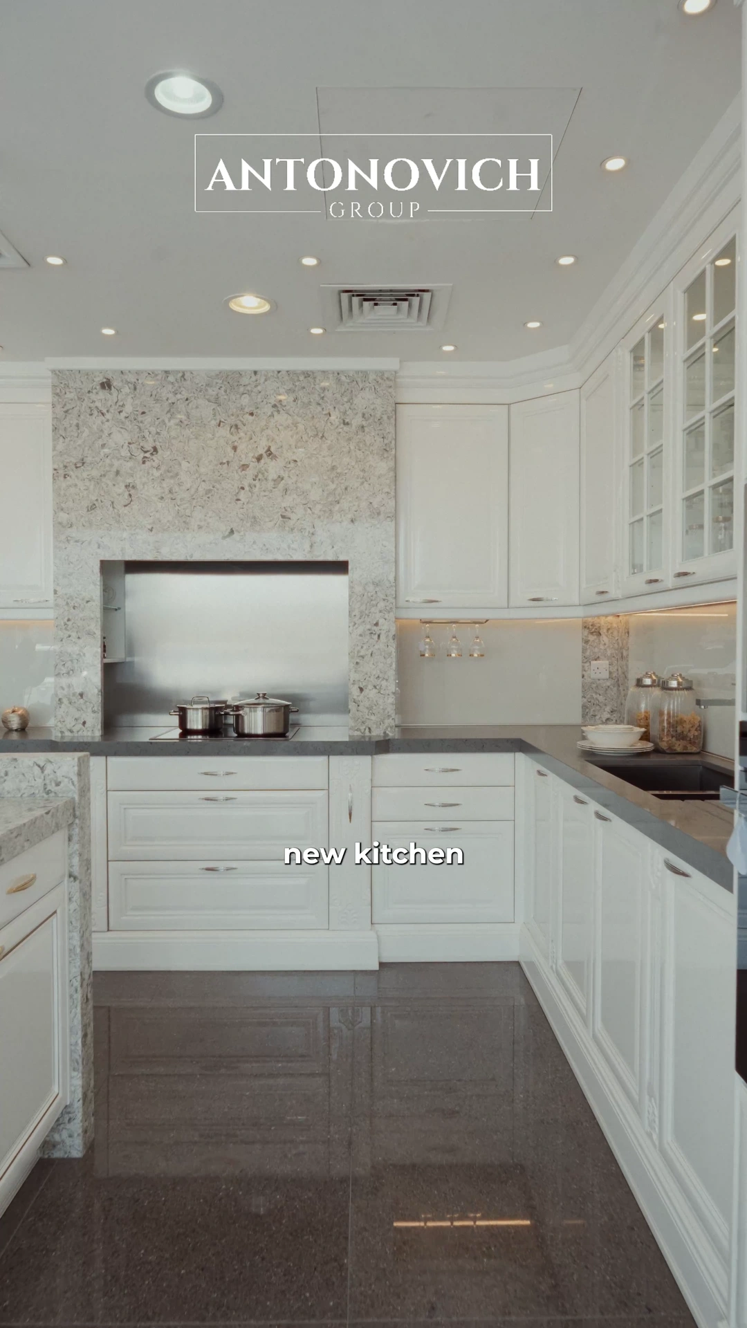 Project manager in a white blazer presenting a classic white kitchen with glazed cabinets and a stone backsplash