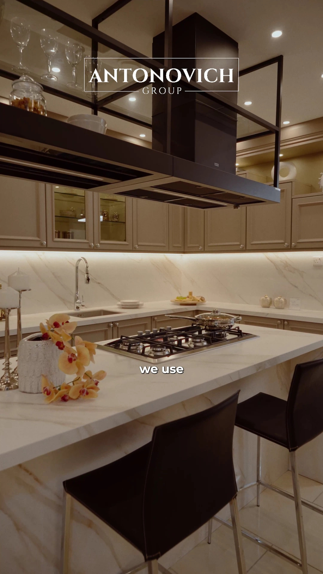 Project manager in a brown suit presenting a grey and white kitchen with an island and a dining table