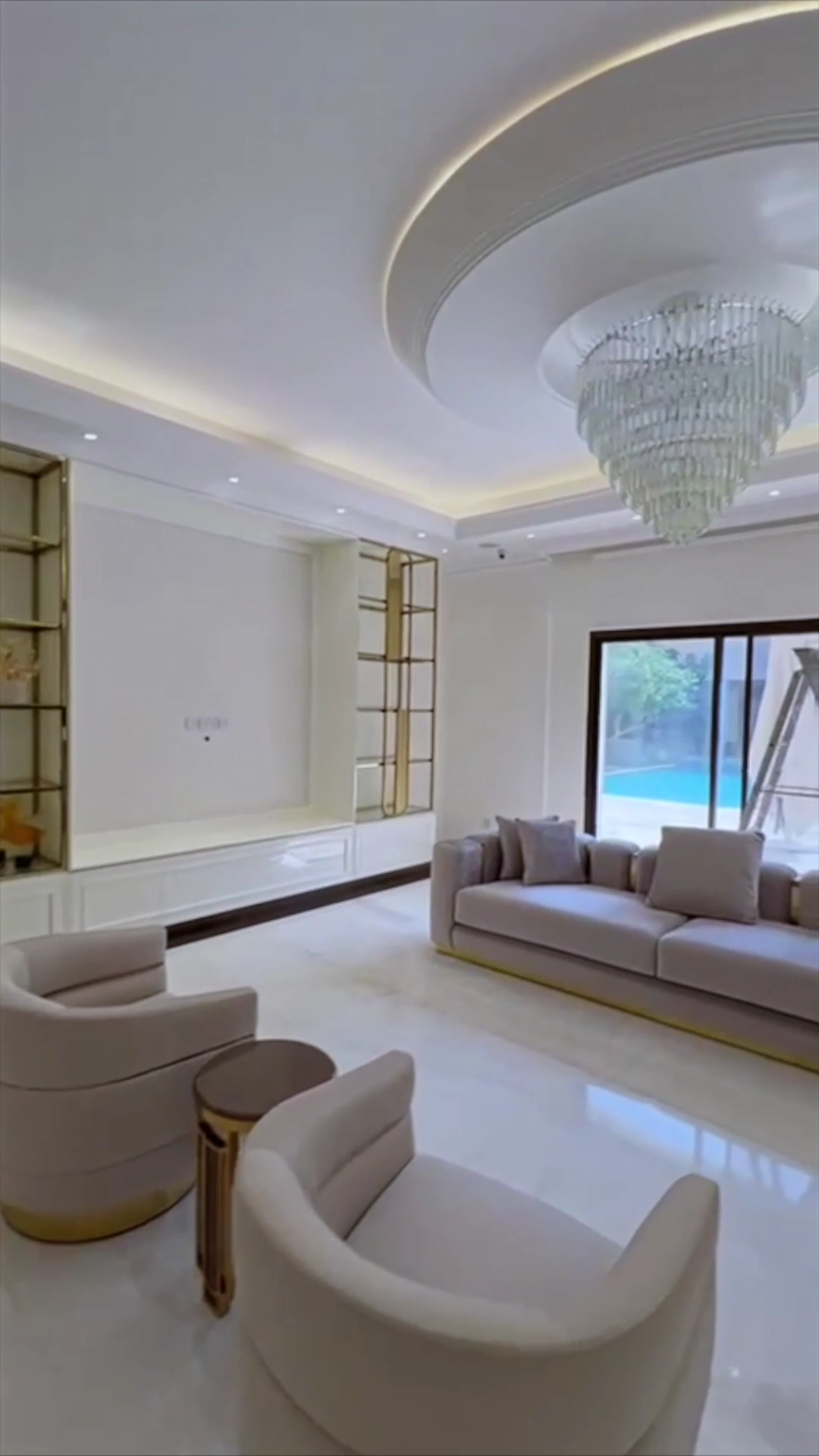 Renovated villa living room in Dubai with a tiered crystal chandelier, gold trimmed shelving and sliding doors onto the pool