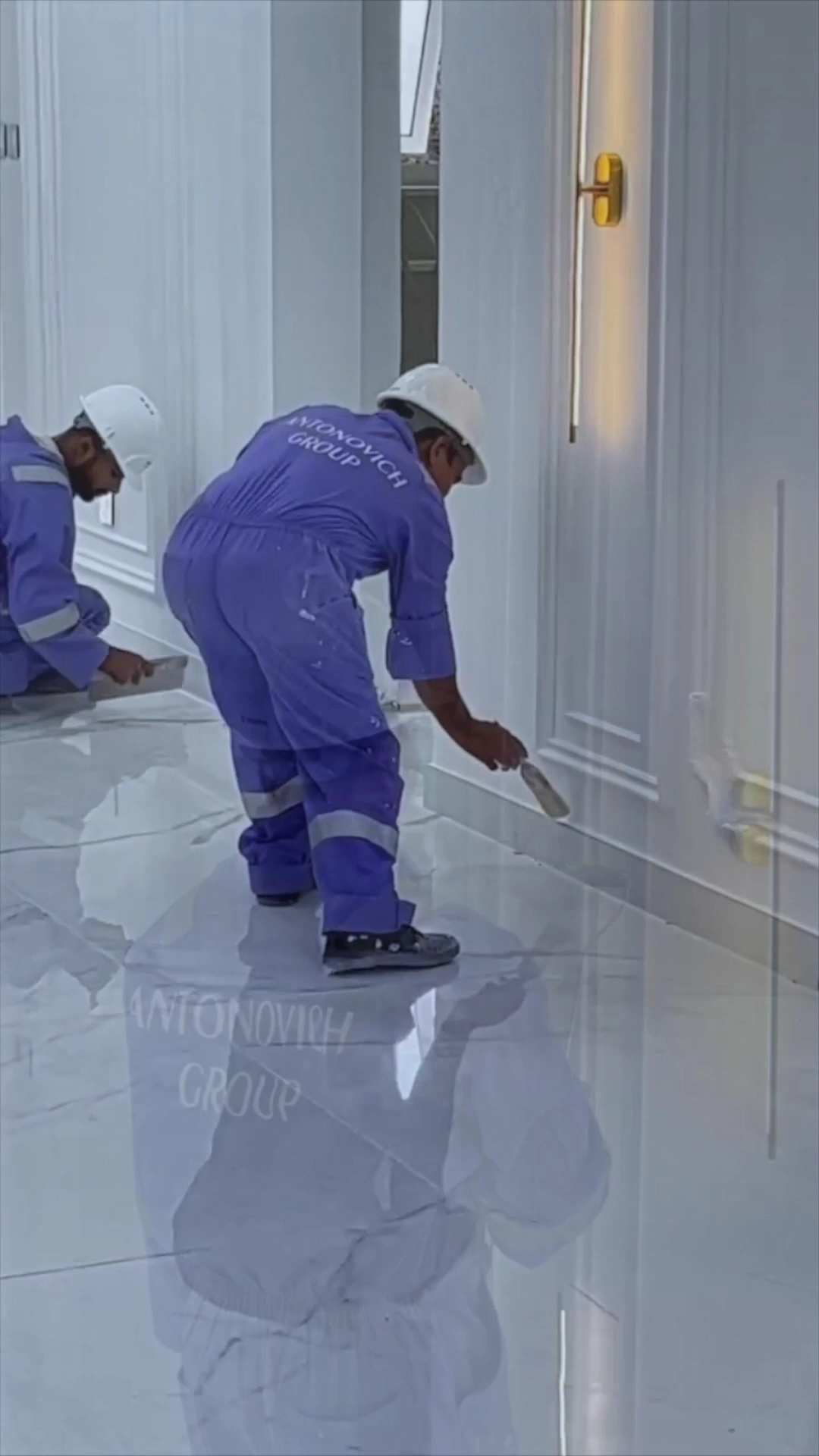 Antonovich Group workers in blue uniforms and white hard hats finishing wall panelling above a polished marble floor in a Dubai villa