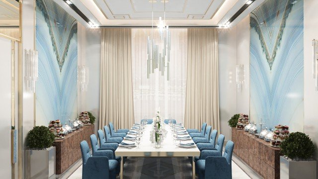 The picture is of a contemporary, luxury living room with floor-to-ceiling windows and views of a city skyline. The room has a white and gray color palette, with a sectional sofa upholstered in soft gray velvet and a glass coffee table. There is also an upholstered armchair, poufs, and a geometric rug in shades of gray. In the center of the room is an upscale modern chandelier.