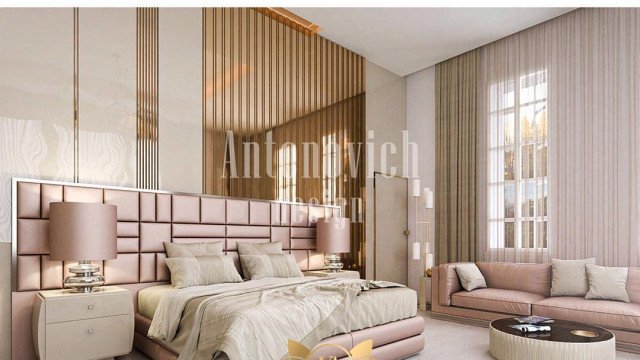 This picture shows a luxurious modern living room with a large sofa, dark wood floor, and crystal chandelier. The furniture is upholstered in a light cream fabric, while the walls and ceiling are painted white and adorned with intricate moldings. On the left side of the room is a large window that looks out onto a garden. There is also a fireplace with a marble surround, a bar area, and a long black coffee table. The overall effect is one of elegance and sophistication.