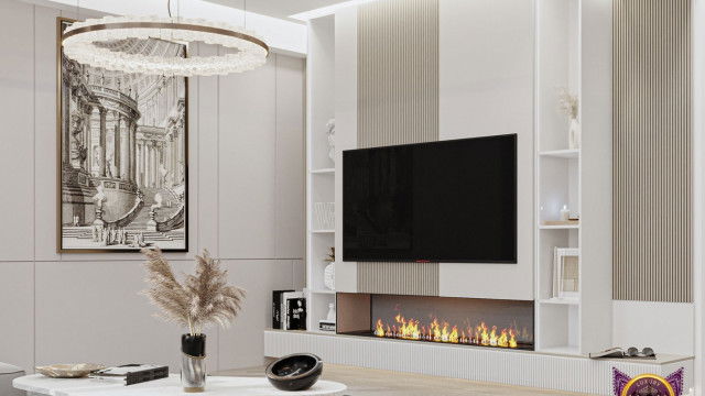 This picture shows a modern, open concept living room. It features a large white sofa, surrounded by two large dark blue armchairs, along with a round, light blue ottoman in the center of the room. The walls are painted pale gray, and a white sliding door leads to an outdoor terrace. A modern white fireplace is on one wall, and a large television is on another. The floor is a marble-look tile in shades of white, black, and gray.