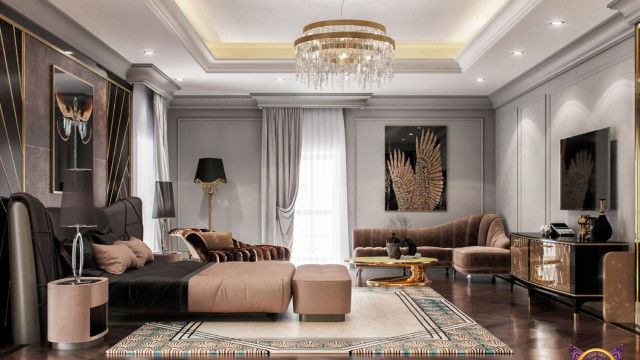 This picture is a rendering of a modern, luxurious living room featuring a sectional sofa in a bold blue velvet upholstery with deep tufting and low profile. A large round silver mirror is mounted on the wall opposite the sofa, along with several modern abstract art pieces. The walls are covered in a light beige wallpaper, and the room is illuminated by two classic black and gold lamps sitting atop two small side tables on either side of the sofa.