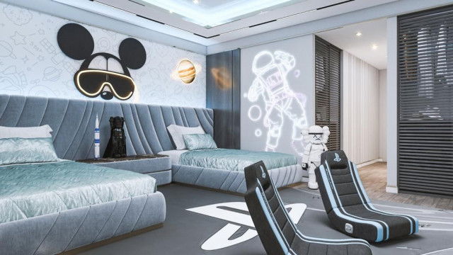 This picture shows a luxurious living room interior. It features a plush cream-colored couch in the center of the room with two matching armchairs on either side. The walls and ceiling feature an elegant paint job with neutral colors and modern light fixtures on the walls and ceiling. The floor is covered in a large, intricately designed area rug with a pattern that resembles a flower. On the walls are several pieces of art, and the room is finished off with a glossy black coffee table and a large plant in one corner.