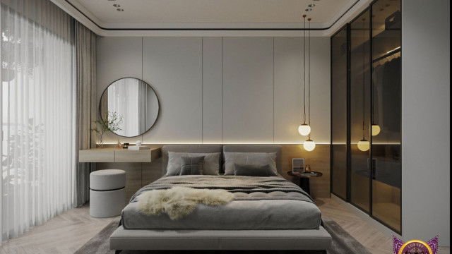 The picture shows a luxurious bedroom designed by Antonovich Design. It features a modern bed with a striped headboard, sleek black nightstands, and a large white and gold area rug. The walls are a beige color with tall cream-colored curtains framing the window. Throughout the room, we can see sophisticated decor such as a gold globe lamp, framed artwork, and a crystal chandelier.