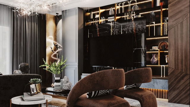 This picture shows a modern living room with a muted color palette. The walls are painted in a light gray and the furniture is upholstered in neutral tones. A black leather sofa sits facing an ottoman in the center of the room. On either side of the sofa are two arm chairs upholstered in a tan fabric. A glass and metal coffee table sits in front of the sofa and adds a contemporary touch to the room. The walls are adorned with abstract art pieces in black frames, and a plush grey rug is placed in the center of the room.