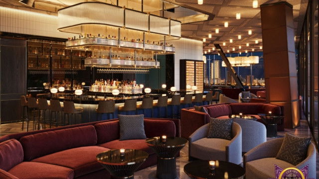 This picture shows a luxurious traditional-style living room. The room has high ceilings, marble floors, and ornate furniture. There is a chandelier, several large sofas, and several side tables with lamps, as well as a fireplace. An antique clock hangs on the wall, and several paintings are displayed on shelves. The overall design is sophisticated and elegant.