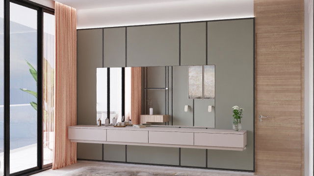 This picture is of a modern bedroom interior designed by Antonovich Design. The room features a large bed with white bedding, a grey tufted headboard, and two bedside tables with white lamps. The walls are painted in a pale grey and there is a large window overlooking the city skyline. The room also includes a grey chaise lounger, an upholstered chair, an ottoman, and an area rug.