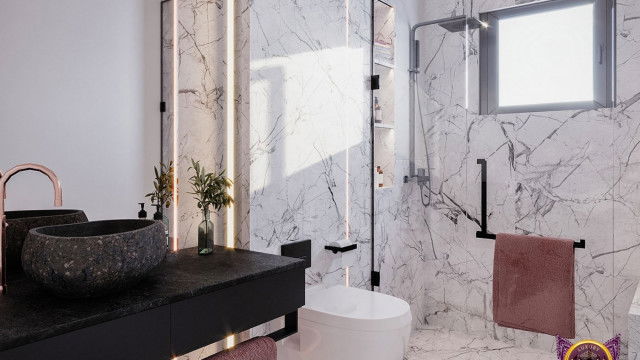 This picture shows a modern, luxury bedroom decor. The room features a large bed with white upholstered headboard, a round nightstand with matching lamp, and two velvet armchairs in a light grey hue. The walls and ceiling are painted a light shade of grey, while the floors are a dark hardwood. The room is decorated with wall art, a large rug, and various decorative objects.