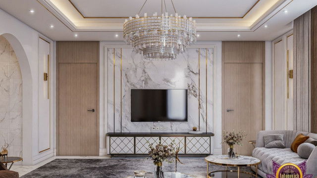 This is an image of a modern luxury living room with a contemporary design. The room features a large couch upholstered in neutral-toned fabric flanked by two armchairs in the same fabric. An area rug lies on the floor, and a glass coffee table stands in the middle of the seating area. The walls are painted a dark color, while the fireplace is white with a geometric tile surround. Accent pieces such as a tablet-shaped wall mirror and a vase add stylish touches to complete the look.