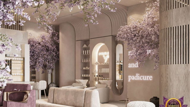 This picture shows an elegant living room with a contemporary design. The room has two dark gray sofas, an ottoman, and a matching armchair in the center. The walls are painted white and there is a large window that looks out onto a balcony. The floor is wood and there is a rug in the center. The room also features a fireplace and built-in shelves.