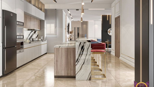 The picture shows a luxurious modern kitchen with marble countertops, stainless steel appliances, and floor-to-ceiling windows. There is a large island in the center of the room with a sink and four bar stools, as well as plenty of storage space. The walls are painted white, and the floor is tiled in a light gray. The room also features several unique lighting fixtures that accentuate the modern style.