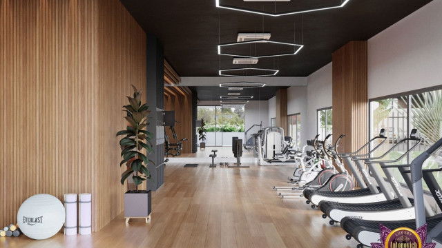 This picture features a modern interior design featuring a white ceiling with recessed lighting. The walls are painted in a light color with a shimmering metallic strip running along the bottom of the wall. The floor is dark and made of hardwood, while the furniture is upholstered in shades of cream and brown. The centerpiece of the room is a large leather sofa with a thin chrome frame, flanked by two modern chairs, and a mid-century style coffee table in the center.