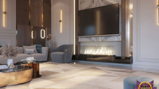 This picture shows a luxurious living room in a modern home. The room is decorated with white walls, gray flooring, and a stone fireplace. There is a beige couch with white and gold accents, an ornate coffee table, and a few accent chairs. On the walls are beautiful, framed artwork and some decorative lamps. The room is completed with a large glass window that overlooks a garden.
