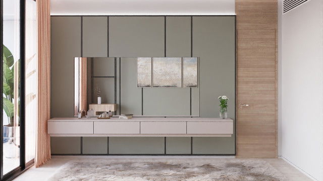 This picture shows a modern living room in shades of white, black and grey. The space is luxurious and features a sofa with patterned cushions and a grey shag rug. To the side there is a round black table with a shiny gold lamp on top. On the other side there is an elegantly designed shelf with items of decor, including a modern vase and a geometric sculpture.