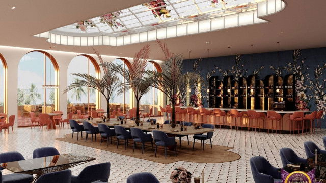 The image shows a luxurious living room with contemporary modern style. The room features a large cream-colored sectional sofa and two white armchairs, all arranged around a large round glass coffee table. The walls are decorated with a large white and gold framed mirror, with a pair of sconces mounted above it. The floor is covered in a cream-colored rug and the room is accented with gold furniture including an end table and a stunning chandelier hanging from the ceiling.