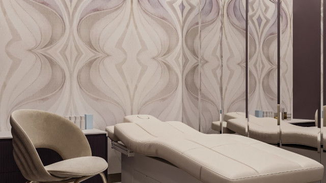 This picture shows an elaborate indoor swimming pool design. A large turquoise pool is situated in the center of the room and is surrounded by a row of tall pillars with ornate accents. A winding staircase leads up to a balcony, which provides a seating area overlooking the pool. Surrounding the pool are walls of windows which provide views of the outdoor garden and the ocean beyond.