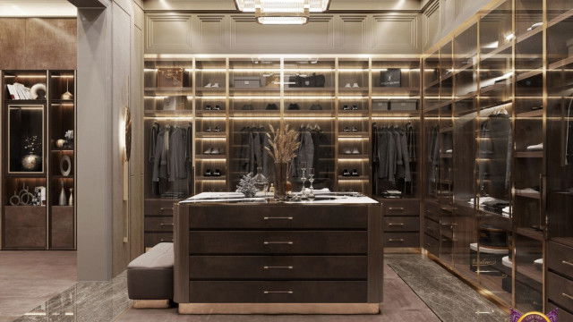 This picture shows an overhead view of an ornately decorated living room. The focal point of the room is a large, circular table surrounded by plush upholstered chairs. The walls are covered in a luxurious paneled wallpaper with light-colored accents and bold artwork. A grand chandelier hangs from the ceiling, and the dark wood floors are accented with a patterned area rug.