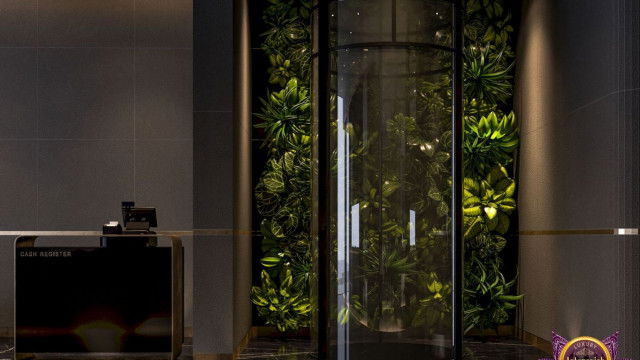 This picture shows an elegant modern living room with a large sofa and two armchairs facing a wooden coffee table. The walls are painted with a light grey color that contrasts with the black furniture, while plenty of natural light is entering the room through the large windows. There are several accent pieces including bright blue cushions, a classic white clock, and a modern pendant light.