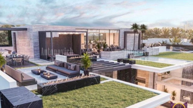 This picture shows a modern living room with a light grey sectional sofa, an accent chair, and a white shag rug. The walls are painted a warm beige color and there is an abstract painting on the wall. There's a small round coffee table in the center of the room and a nearby side table with a modern lamp on it.