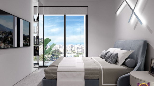 This image is of a modern living room designed by Antonovich Design. The room features a light grey sectional sofa paired with two turquoise accent chairs. The walls are painted a soft white shade, and the ceiling has recessed lighting. A black marble fireplace with a built-in media console is a focal point in the room, and the floor is covered with a light grey carpet. There is a large glass window looking out over a pool and a garden.