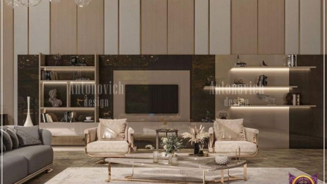This picture shows a modern and luxurious living room design. It includes a white L-shaped sofa with gold accents, a glass top coffee table, a plush area rug, and a large flat-screen television mounted on the wall. The walls are painted a light gray color and there are several large windows for natural light. At the center of the room is an elegant crystal chandelier with cascading lights.
