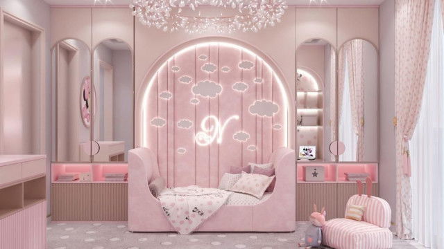 This picture shows an outdoor living space designed by Antonovich Design. It features a long wood and stone table with several matching chairs situated in a lush, green garden. The area is surrounded by tall, pinewood fences and accompanied by a few stone columns and a water fountain in the background. The overall design is quite modern and elegant, creating a cozy atmosphere for outdoor entertaining.