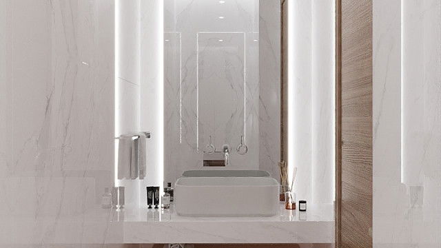 This picture shows a luxurious, modern living room designed by the firm Antonovich Design. The room features a large white sofa and ottoman with a statement mirror above it, along with stylish gray armchairs and a glass top coffee table. There is also an ornate rug and fireplace as well as a small display of decorative accessories on the shelves. The ceiling features a stunning chandelier and plenty of natural lighting coming in from the large windows.