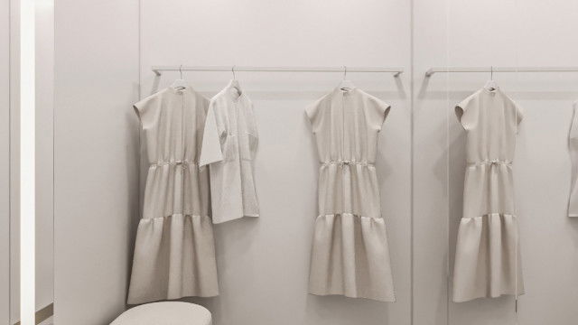 This picture shows a modern living room with a gray and white color palette. The room features a large sectional couch, set in front of a striking wall mural featuring abstract shapes and patterns. The walls are lined with white built-in shelving and lighting fixtures, and the floors feature light wood-look tile. An accent chair and an oversized ottoman are situated off to the side, and the room is decorated with colorful framed artwork and greenery.
