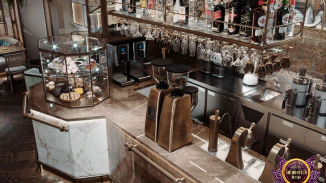 This picture shows a modern, luxury living room designed by Antonovich Design. The room has a white marble floor, with a brown leather sofa to the left and a small glass coffee table in front of it. The walls are painted a light gray color and have several framed art pieces hanging from them. In the center of the room is a white chandelier that hangs down from the high ceiling. There are also two gray armchairs to the right of the sofa and a white mantel with a small fire burning inside.