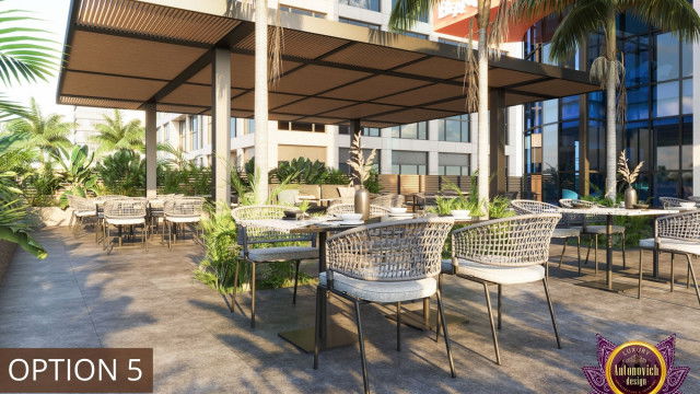 This is a picture of a modern, contemporary living room designed by Antonovich Design. The room features a white interior with touches of grey, gold and black accents. There is a white sofa set that sits in the middle of the room, with black and gold throw pillows and a sleek, white chair. On the other side of the room is a white entertainment center with two flat screen TVs framed in black. Above the sofa is a contemporary art piece in a golden frame. In the corner of the room is a tall, white bookshelf for additional storage, as well as a
