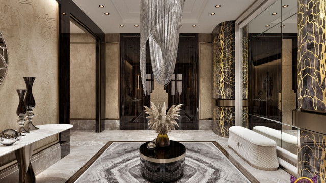 This picture shows a luxurious living room with modern decor accents. The walls and floor feature light grey and white marble tiles, while the furniture is upholstered in a sandy beige fabric. In the center of the room is a large, off-white sectional sofa, paired with a glittering glass coffee table and two navy velvet armchairs. A silver chandelier hangs from the ceiling, illuminating the room. Finally, there are two end tables with gold accents and a decorative rug that ties the whole look together.