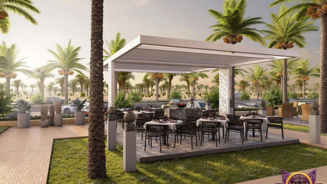 This picture shows an elegant and sophisticated living room interior. It features a plush light blue velvet sofa with a white patterned throw blanket draped across the back. The walls are a light gray color with ornate scroll patterns along the sides. An abstract painting hangs above the sofa, adding another level of interest to the design. On the left side of the room is a glass top coffee table and two matching chairs, while on the right side is a white tufted ottoman with decorative throw pillows. In the background, large windows allow natural light to pour in, illuminating the space