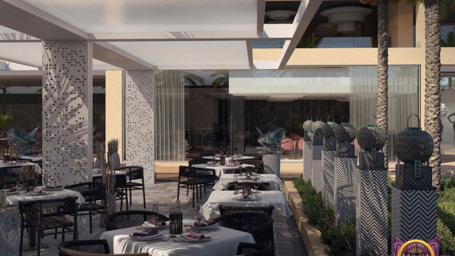 The image shows an elegantly decorated living room with glossy hardwood floors, a white and gold sofa set with plush cushions, a round glass-top coffee table, and a pair of floor-to-ceiling windows overlooking the city skyline. The walls have a light beige tone to them and there is a pale grey area rug in the center of the room. There are numerous pieces of modern art decorating the walls, and the ceiling is decorated with crystal pendant lights.