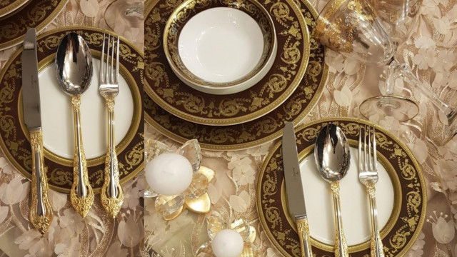 This picture is of a modern luxury living room. The room has a neutral color palette with white walls and furniture. There is a black marble fireplace in the center of the room with two large white sofas on either side. There is a glass coffee table and an abstract art piece hanging above the fireplace. The room also features rich wooden accents against the white walls and along the room's edges. The room has a formal and inviting atmosphere.