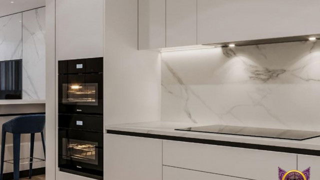 This picture shows a modern, minimalist kitchen featuring a built-in stainless steel oven, a sink with a contemporary black faucet, and a white quartz countertop with a gray marble backsplash. There is also a gray tile floor and a large window with sheer curtains allowing natural light to fill the space.