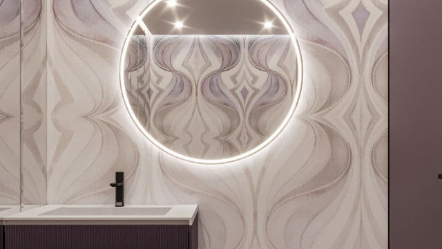 This picture appears to be a luxurious and contemporary lobby area with a sweeping marble staircase. The walls are lined with tall, gold-framed oil paintings and very high, rounded windows. There is a seating area with two velvet chairs, a round marble side table, and a circular mirror above the fireplace. The floors are inlaid with an intricate and eye-catching pattern of different varieties of marble.