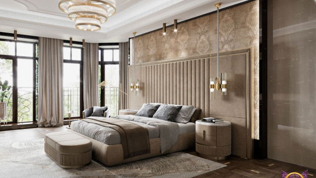 The picture shows a modern bedroom with an upscale design. The room features a light grey wall and a white ceiling. There is a large window with a sheer white curtain that lets in a lot of natural light. The bed has a white upholstered headboard and footboard, and white bedding. The nightstands are also white with brass accents. On the walls, there are patterned wallpapers in neutral colors that match the rest of the decor.