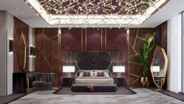 This picture shows an ornate picture frame with an intricate design. The frame is painted a dark shade of red and decorated with gold accents. Behind the frame is an upholstered seating area with a white-on-black patterned throw pillow. In the background there is a tall candle holder adorned with several votives.