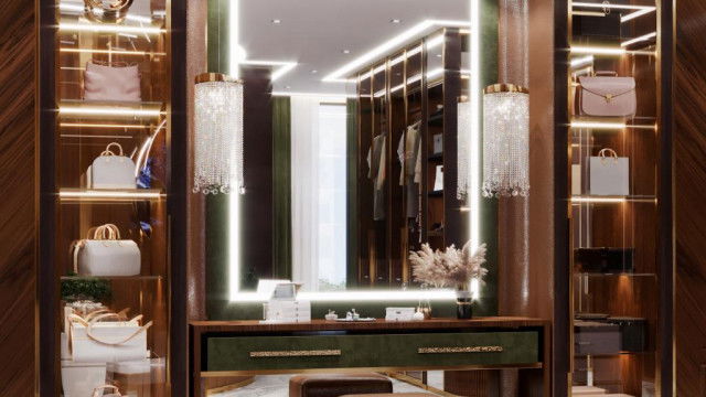 This picture shows a contemporary living room in an elegant home that features modern style furniture and décor. The room is decorated in shades of grey and white, with a large abstract painting on the wall. There is a white sectional sofa, as well as a grey armchair and ottoman, both of which feature angular lines and geometric shapes. The walls and ceiling have built-in lighting, and there is a white fur rug and a glass coffee table in the center.