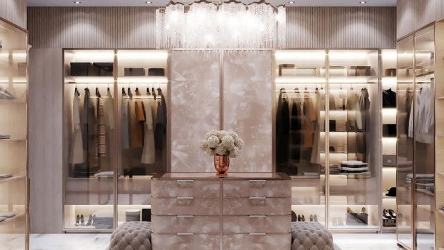 This picture shows a luxurious and modern living room interior. The room is decorated in shades of grey and white, with furniture upholstered in velvet. There is an ornately carved fireplace mantel and a large floor-to-ceiling window that allows plenty of natural light to enter the room. The space is also furnished with a crystal chandelier, a plush sofa, and two armchairs.