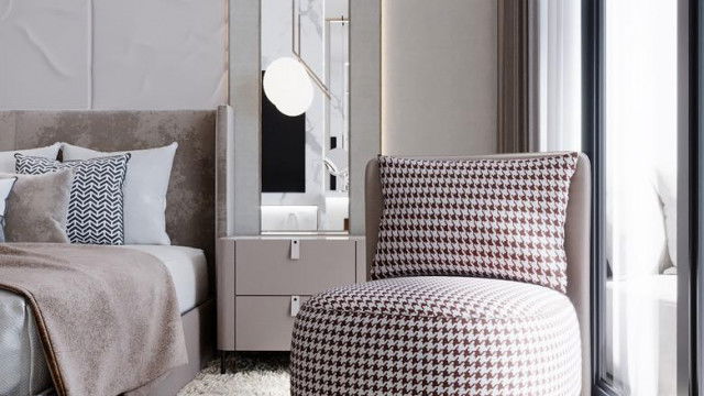 The picture shows a luxury living room with modern decor. The furniture is dark wooden and includes a sofa, two chairs, an ottoman, and a coffee table. The walls are a light beige color and there is abstract art hanging on the wall. The lighting fixtures are suspended from the ceiling and have a sleek, contemporary design.