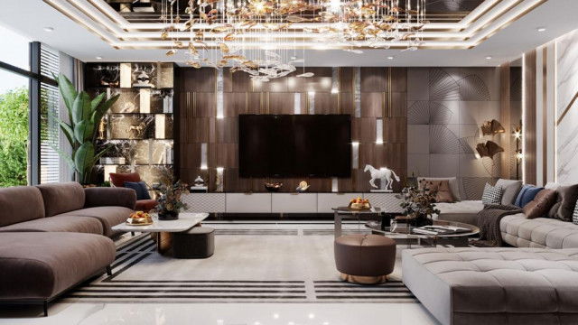 The picture shows a modern living room design featuring an oversized light gray velvet sectional sofa, a round glass coffee table, and white accent chairs. The walls are painted a soft shade of beige, and two large windows with sheer white curtains allow natural light to flood the area. A large abstract painting hangs on one wall, while a geometric rug in shades of gray, white, and navy ties the entire room together.