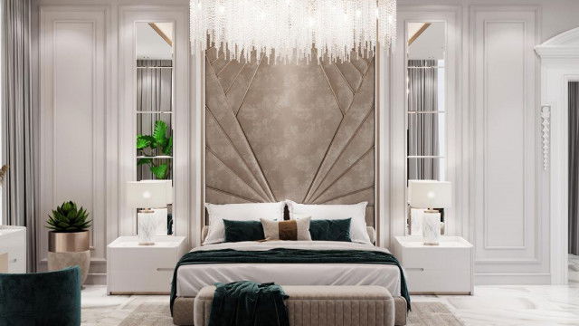 The picture shows an interior design featuring a modern living area with a sleek brown leather couch and matching armchair. The walls are painted in a white color, and there is a long black and gold coffee table in the middle of the room, which is placed in front of two tall marble-effect columns. The floor is covered in dark, patterned carpet and there is a large window with white curtains, allowing natural light to fill the room. On the wall opposite the couch is a large abstract painting, adding a touch of color to the space.