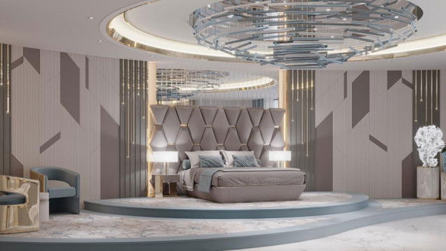 In this picture, we can see a large, contemporary living room with a brown leather sofa, white armchairs, and a matching ottoman around a large glass-top coffee table. There are also several abstract art pieces on the walls and a white fireplace in the corner. The floor is covered in a large area rug and there is an array of potted plants to add a touch of greenery. Overall, the room has a modern yet comfortable feel.