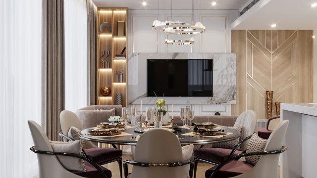 The picture shows an expansive, luxurious living room with a beige, grey, and gold color palette. The room features a large, white leather sofa and two matching armchairs, which are placed around a round, gold-colored coffee table. There is a white fireplace with a gold inlay above it, and two light-colored area rugs are placed on the floor, along with a dark wooden sideboard. There is a tall, arched window that lets in plenty of natural light, and the walls are decorated with various art pieces.