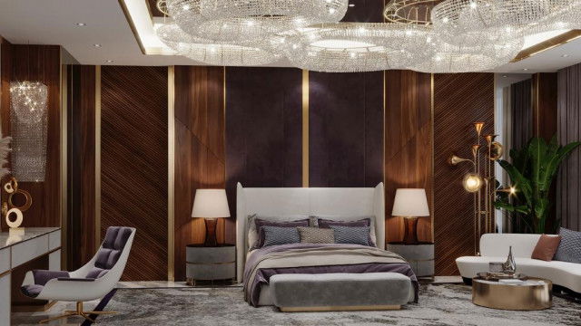 This picture is of a contemporary home office space designed by Antonovich Design. The design features a desk with a geometric patterned wall behind it, an armchair with a sleek wooden frame, and a large window with white curtains. There are several storage compartments, including an overhead shelf, beneath the desk and a smaller shelf behind the chair. The colors used in the design are predominantly neutral, with the white, beige, and grey hues bringing a sense of calmness to the space.