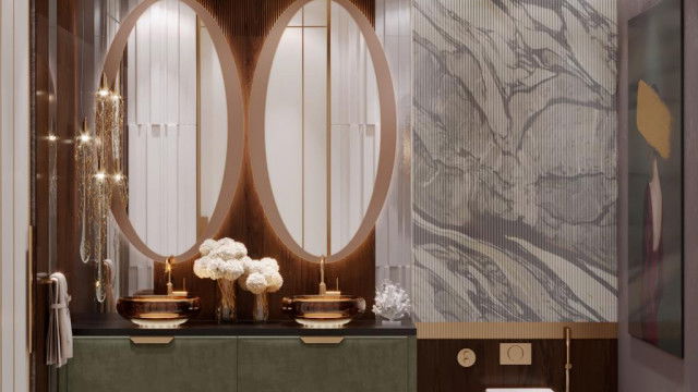 This picture shows a luxurious bedroom with a graceful, classic design. The walls are painted in a light shade of yellow and the furniture is gold-toned and ornately detailed. The bed is dressed with a light blue and white bedspread and a separate bed skirt with a floral pattern. There is a golden mirror atop a mahogany dresser and two poster beds to each side of the bed. On the wall behind the bed is a landscape painting with shades of green and brown. A white nightstand and two small chairs with green upholstery complete the scene.