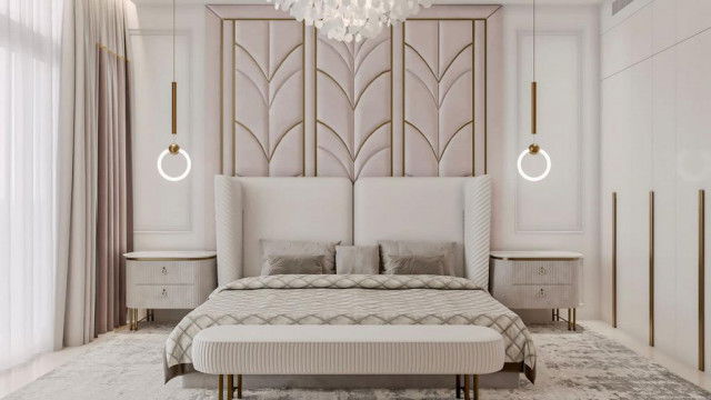 This picture shows an opulent and luxurious bedroom, featuring a dramatic four-poster bed with a deep blue velvet canopy and matching drapes. The walls are covered in a light cream wallpaper with metallic gold accents, and the floor is finished in glossy dark hardwood. A chaise lounge sits at the end of the bed, and there are several elegant accents scattered about the room, including a crystal chandelier and an ornate, gilded mirror.